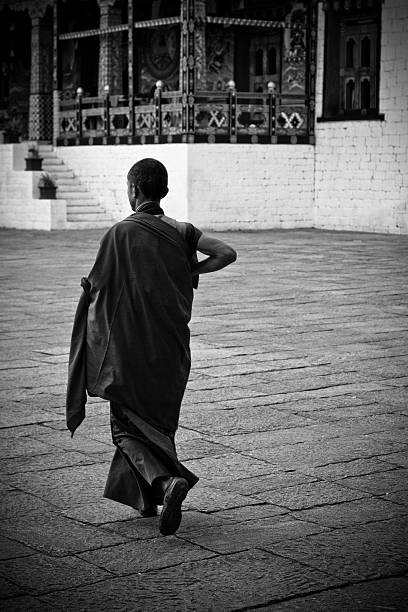Novice monk of the Tashi Chho Dzong Fortress, Thimpu, Bhutan Thimpu, Bhutan - October 25, 2014: Young novice Buddhist monk walk the courtyard in The Tashi Chho Dzong Fortress, Thimpu, Bhutan black and white travel travel destinations monk stock pictures, royalty-free photos & images