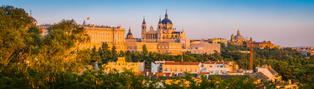 Madrid Almundena Cathedral and Palacio Real sunset cityscape panorama Spain Golden light of sunset illuminating the ornate domes and spires of the Almundena Cathedral and classical facade of the Palacio Real across the rooftops of central Madrid, Spain's vibrant capital city. ProPhoto RGB profile for maximum color fidelity and gamut. madrid city view stock pictures, royalty-free photos & images