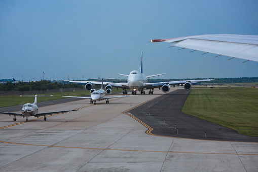 Airplanes big and small lining up on runway for taking off at a busy airport