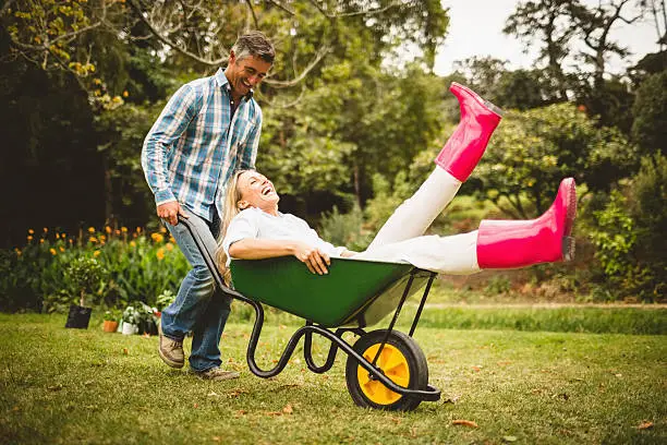 Happy couple playing with a wheelbarrow on a sunny day