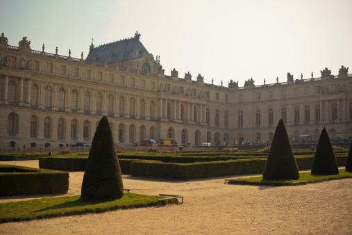Versailles, France - March 13, 2014: A back lit shot of the Palace of Versailles in Versailles, France. People can be seen walking around in the Gardens of the Palace of Versailles on an early spring day. The tourists can be seen walking around the gardens in front of a backlit Palace used by Louis XIV during his reign.