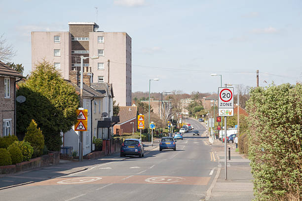 light traffic suburban streetscene in the town of Harlow England Harlow, United Kingdom - March 24, 2014: In the Potter Street area of Harlow Town in Essex, England, a view of traffic on Potter Street at the junction of Southern Way. The road is bathed in bright spring sunshine,  and the tower block apartments of Brenthall Towers are  in the middle ground. Light traffic uses the road and a few pedestrians can be seen close to the local shopping centre, in the 20 mile per hour speed limit.    harlow essex stock pictures, royalty-free photos & images