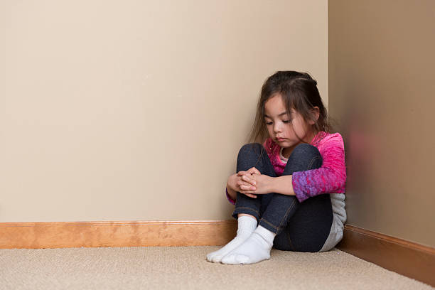 Child in Corner looks like a timeout / or maybe she is thinking / of what to play next hugging knees stock pictures, royalty-free photos & images