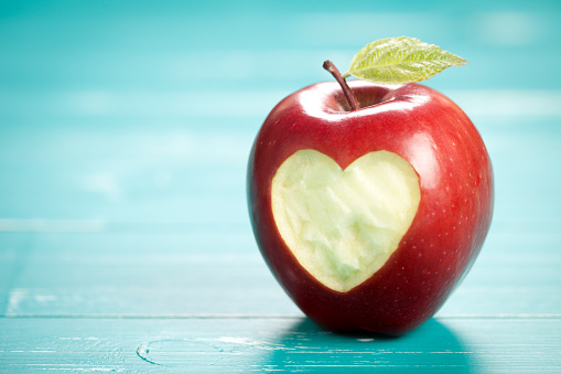 Apple with heart on turquoise table. On left side is empty space to put text or something else. This file is cleaned and retouched.