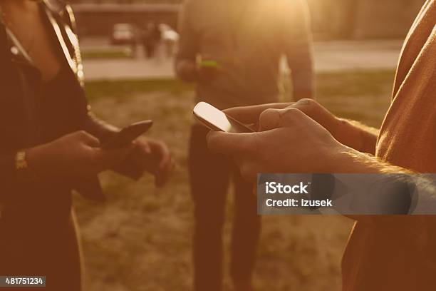 Friends Using Smart Phones Outdoor At Sunset Stock Photo - Download Image Now - 2015, Adult, Bonding