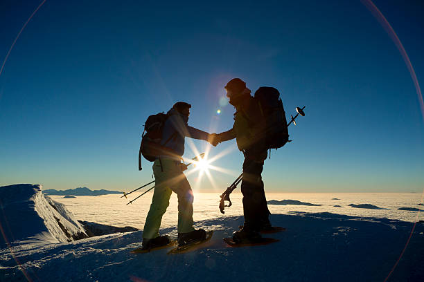 два путешественников встряхивая руки на снежный пейзаж с покрытием - snowshoeing hiking mountain winter стоковые фото и изображения