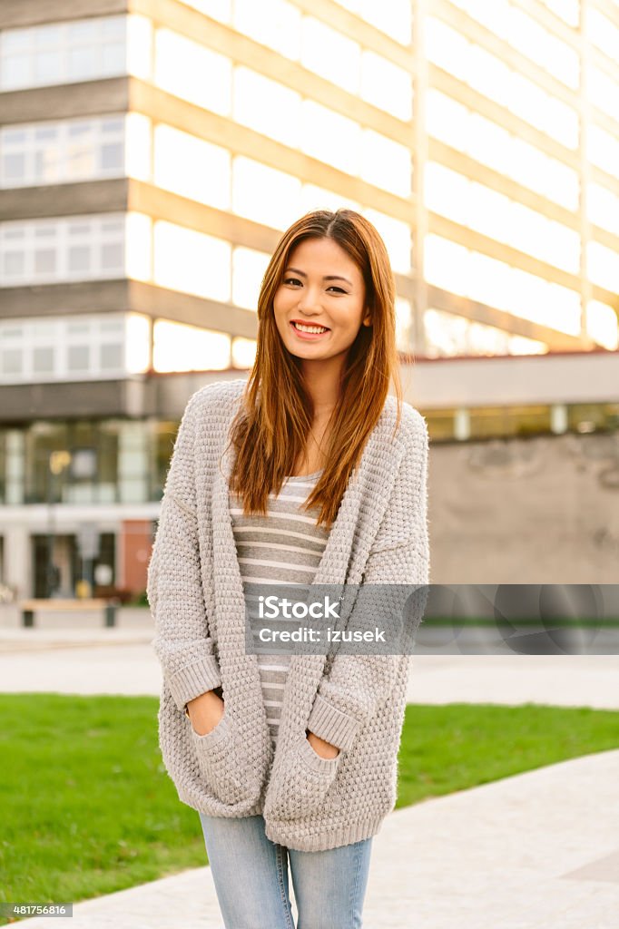 Outdoor portrait of beautiful asian young woman Outdoor portrait of beautiful asian young woman wearing cardigan, standing in front of building at sunset and smiling at camera. 20-24 Years Stock Photo