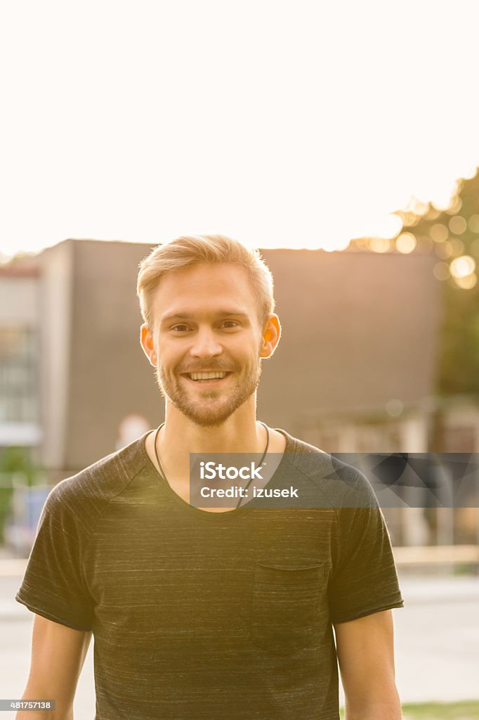 Outdoor portrait of handsome bearded blond hair young man Outdoor portrait of blond hair handsome bearded young man standing in front of building at sunset, smiling at camera.  20-24 Years Stock Photo