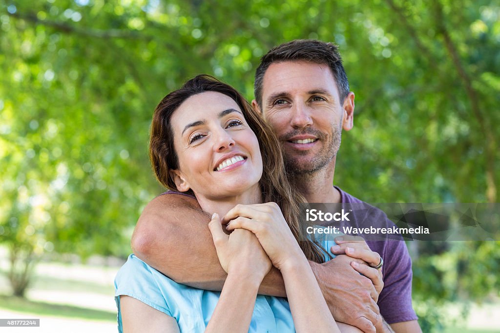 Feliz pareja sonriendo a la cámara en un parque - Foto de stock de 30-34 años libre de derechos