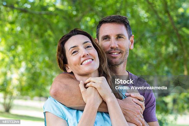 Feliz Pareja Sonriendo A La Cámara En Un Parque Foto de stock y más banco de imágenes de 30-34 años - 30-34 años, Pareja de mediana edad, Parejas