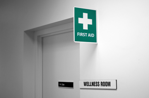 First aid sign, with the wellness room sign on a white wall.