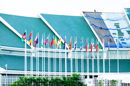 Bangkok, Thailand - November 10, 2014: Flags outside of United nations building in Bangkok. On top of roof a thai worker is sitting. Roof is under restoring works.