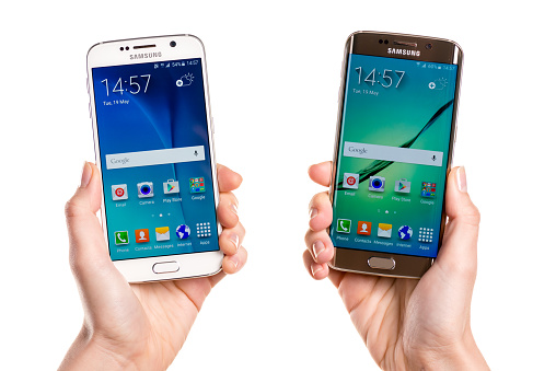 Koszalin, Poland - May 18, 2015: Close-up shot of white Galaxy S6 and gold Galaxy S6 Edge hand-held by woman. Devices displaying the applications on the home screen. Galaxy series phones S6 is made of glass and metal. S6 Edge is the first phone on the market with a curved screen on both sides.
