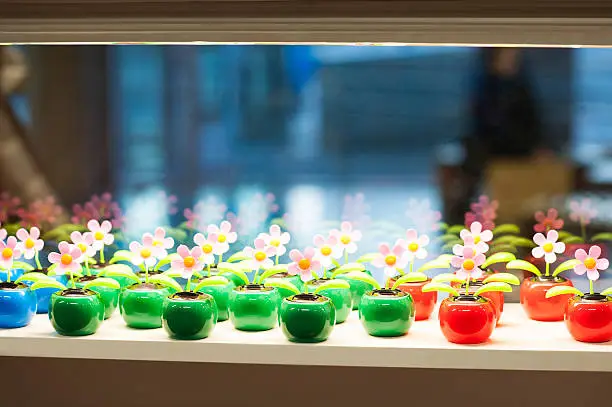 Many identic plastic colored toy flowers on glass shop window.
