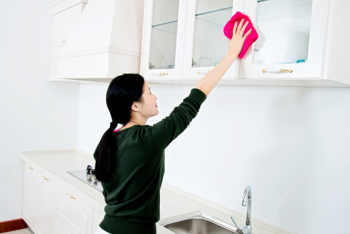 Asian young housewife cleaning the kitchen with a pink cloth.