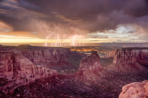 Dramatic lighting and clouds during sunset on the famous Colorado National Monument in Western Colorado near Grand Junction.  The feature is Independance Rock at the center of the image.  City lights of Fruita, Colorado are in the valley below.