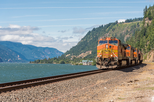 Underwood, Washington, USA - July 21, 2015: A view of a BNSF Burlington Northern Santa Fe railroad Freight train along the Columbia River in Washington State. This includes The front of the Train, a blue sky, the Columbia River and the Washington and Oregon forested hill background. Trains along this river are a Controversial subject. This is near the towns of White Salmon, Washington State and Hood River, Oregon.