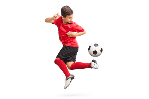 Studio shot of a junior soccer player performing a trick with a soccer ball isolated on white background