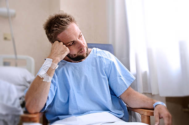 man patient in hospital room sitting alone in pain sad stock photo