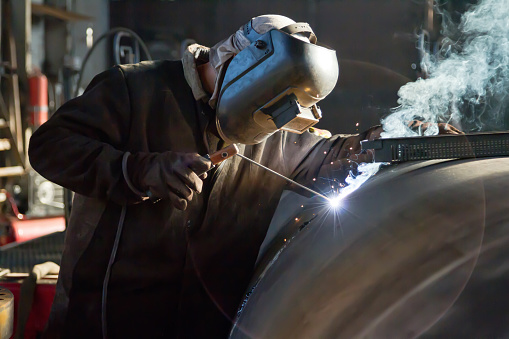 Worker in protective mask welding pipe in workshop