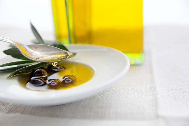 Glass jug with olive oil and scattered olives on black mirror background, low key photo