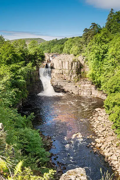 High Force Waterfall on a sunny day viewed from the south bank of the River Tees on the Pennine Way in woodland