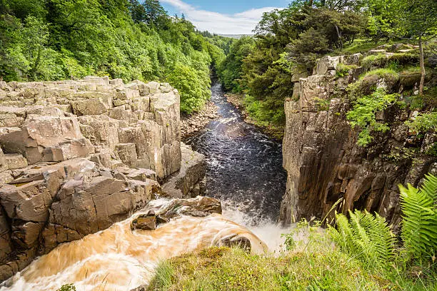 High Force Waterfall on a sunny day viewed from the south bank of the River Tees on the Pennine Way in woodland