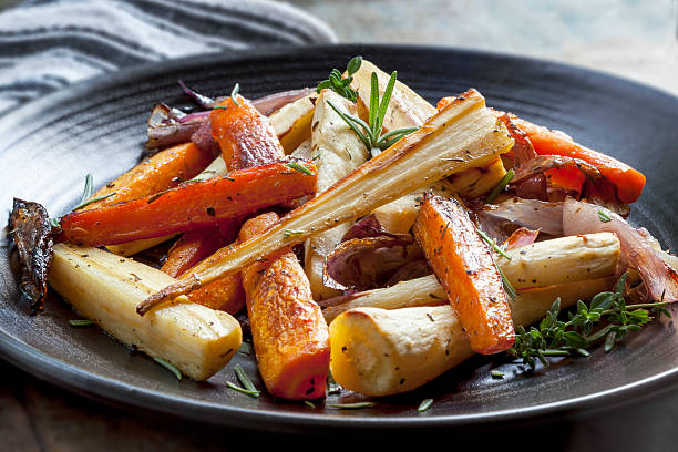 Roasted Root Vegetables Roasted root vegetables on a black serving platter.  Carrots, parsnips, turnips, red onions, and herbs. root vegetable stock pictures, royalty-free photos & images