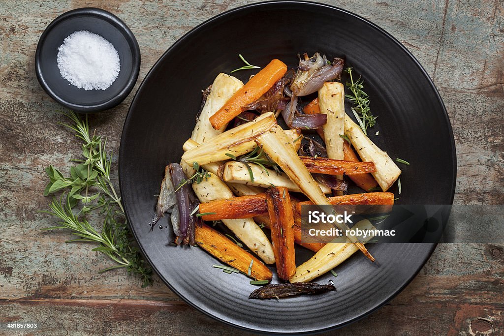 Roasted Root Vegetables Roasted root vegetables on a black serving platter.  Carrots, parsnips, turnips, red onions, salt, and herbs.  Overhead view.Roasted root vegetables on a black serving platter.  Carrots, parsnips, turnips, red onions, and herbs. Baked Stock Photo