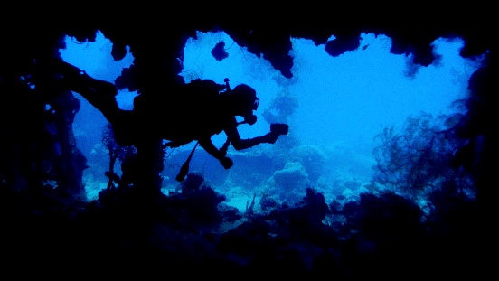 Diver with light passing by opening in sunken ship wreck.