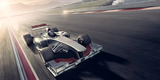 A mid action image of a generic open-wheel single-seater racing car racing car driven by a professional racing driver during an auto sports event during a race. The action takes place on a generic race track near mountains and the sea at evening under a bright sunset. With motion blur on the racetrack. With copyspace. 