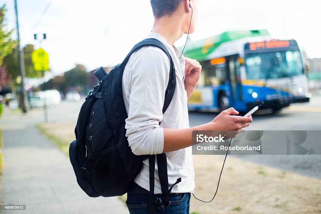 Guy Waiting for the Bus A side view of a young man waiting for the bus while listening to music on his phone. Bus Stop Stock Photo