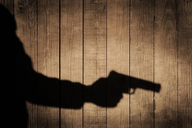 istock Outstretched arm with a gun. Black shadow on wooden background. 481881845