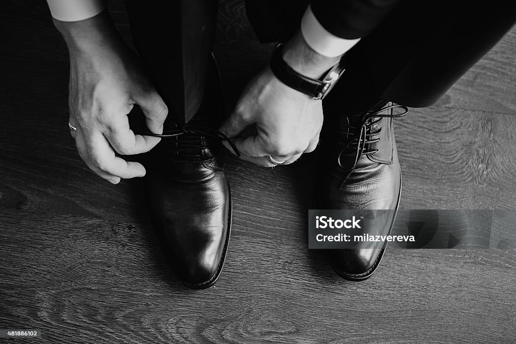 Business man dressing up with classic, elegant shoes. Groom wearing Business man dressing up with classic, elegant shoes. Groom wearing shoes on wedding day, tying the laces and preparing. Black and white photo 2015 Stock Photo