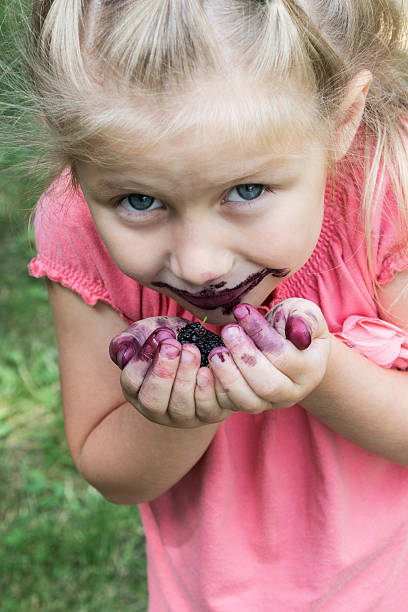 Little girl smeared her face is while eating mulberry on a grass background