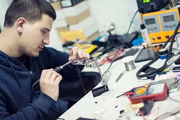 Electronic Technician Worker Soldering Elements on Microchip Circuit Board. A man works at a workstation, soldering together some electronic components.