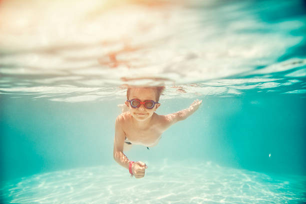 Portrait of smiling little boy enjoying underwater swim in the pool towards the camera. Sunny summer day. Slightly soft.