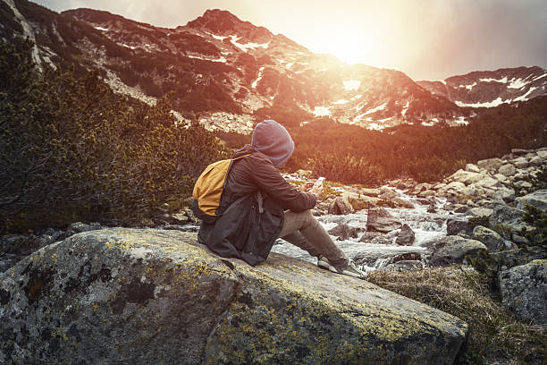 istock Traveler with backpack sitting on a big stone with smartphone 481931250