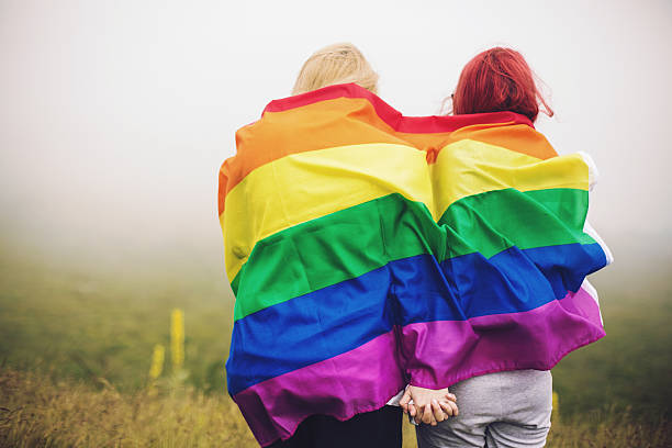 ブロンドと赤毛の女性に包まれたレインボーフラグ - homosexual rainbow gay pride flag flag ストックフォトと画像