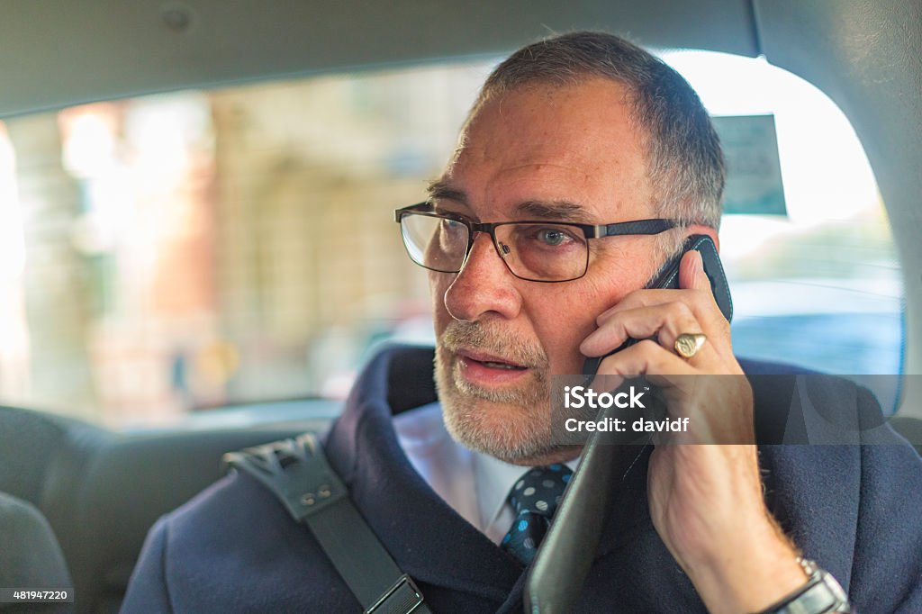 Well Dressed Senior Man On Phone In London Taxi Well dressed smiling senior man talking on a mobile phone while travelling in a London taxi cab 2015 Stock Photo