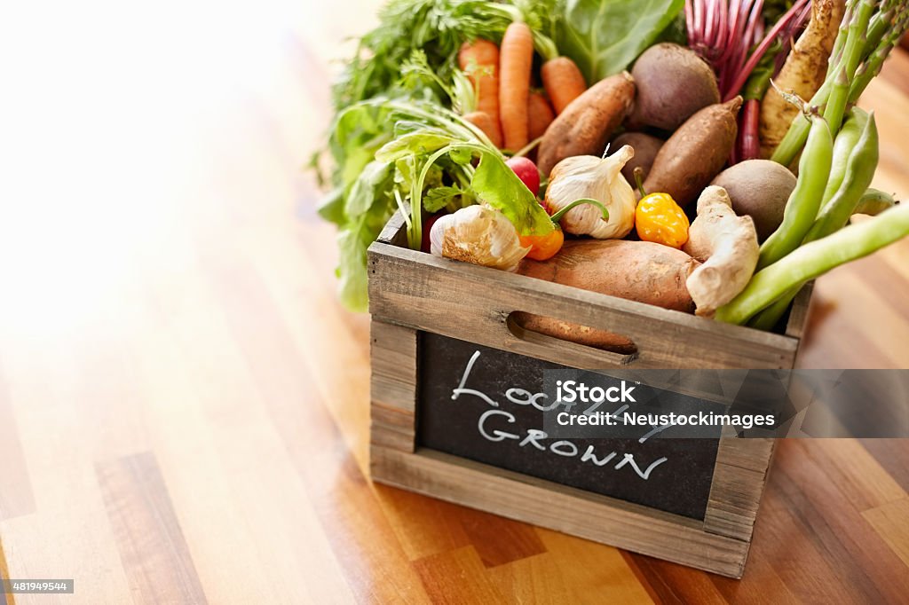 Homegrown vegetables in wooden crate at kitchen High angle view of homegrown vegetables in wooden crate. Text is written on container. Wood box is placed on table. It is in domestic kitchen. 2015 Stock Photo