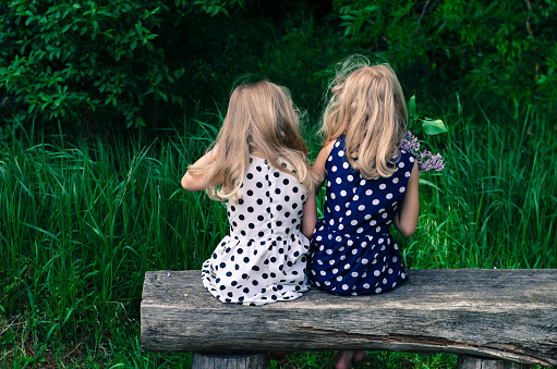 two  blond girls sitting on bench back view