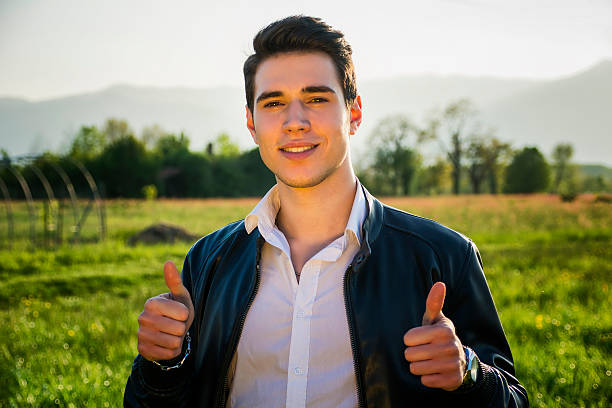 beau jeune homme à la campagne, en face du terrain ou - hand sign human hand ok sign grass photos et images de collection