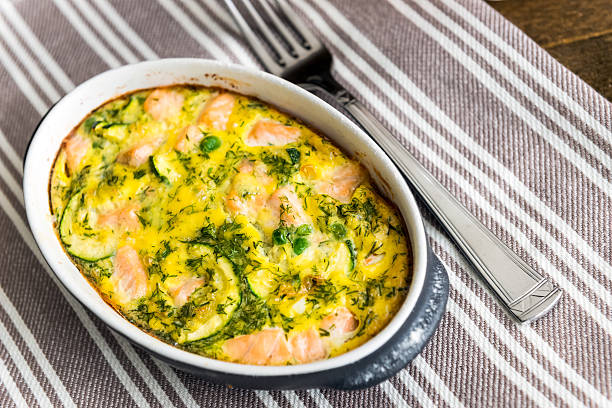 Salmon clafoutis in the oval baking pan. View from above Salmon clafoutis in the oval baking pan on the linen napkin. Fork is close. View from above clafoutis stock pictures, royalty-free photos & images