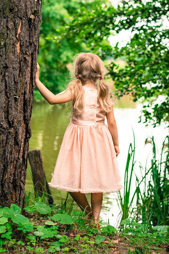 little blond girl with long hair looking to the pond