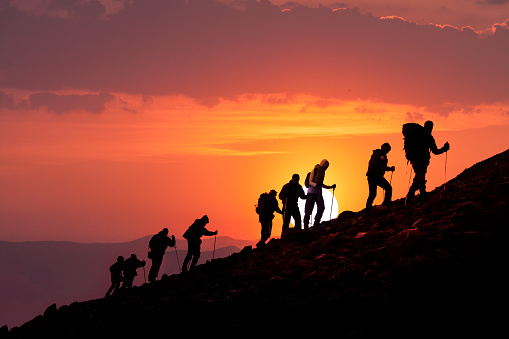 Silhouettes of hikers climbing the mountain at sunset.