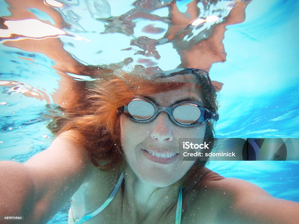 Smiling Woman Taking Selfie Underwater In Pool A smiling woman taking a self portrait underwater in a swimming pool. One Woman Only Stock Photo