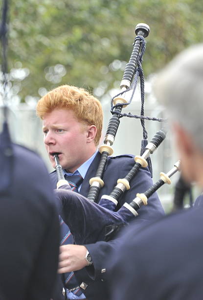 Glasgow, Scotland, UK - August 15, 2014: red haired piper tuning up at world pipe band championships with other pipers and in soft focus in foreground.