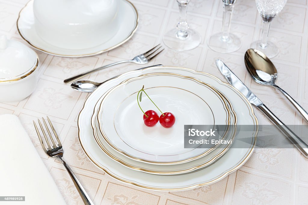 Two cherries lie on a white porcelain plate Beautifully decorated table with white plates, crystal glasses, linen napkin, cutlery and tulip flowers on luxurious tablecloths 2015 Stock Photo