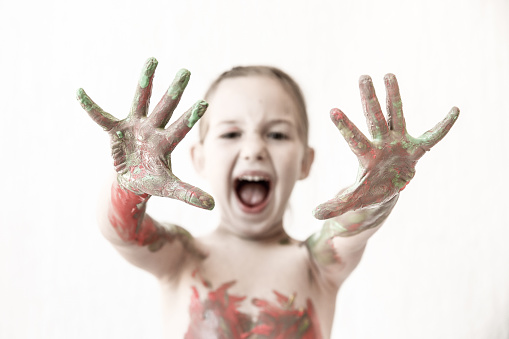 Little girl showing her hands, covered in finger paint after painting her body with it. Playfulness, creativity, permissive parenting, fun childhood concept, selective sharpness, desaturated.